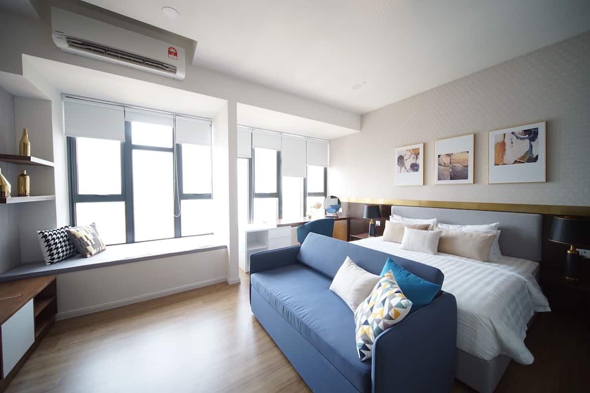 Una habitación de hotel moderna con una cama grande, un sofá azul, un escritorio y un asiento junto a la ventana.