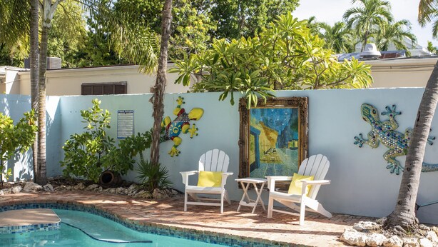 A swimming pool area with a tiled edge, two white chairs with yellow cushions, and decorative wall art including a lizard and a painting of a tropical scene. - Bimini suite-3 bedroom 3 bath, a block off Duval St w/pool, parking (Key West)
