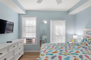 Un dormitorio con cama, cómoda, televisor y ventanas.