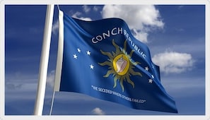 Una bandera con el texto "CONCH REPUBLIC" y el lema "WE SECEDED WHERE OTHERS FAILED" sobre un cielo azul con nubes.