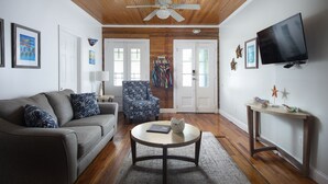 A living room with a wooden ceiling, a gray sofa, a patterned armchair, a round coffee table, and a television mounted on the wall. - Paradise Island suite-2 bedroom 1 bath, a block off Duval St w/pool, parking (Key West)