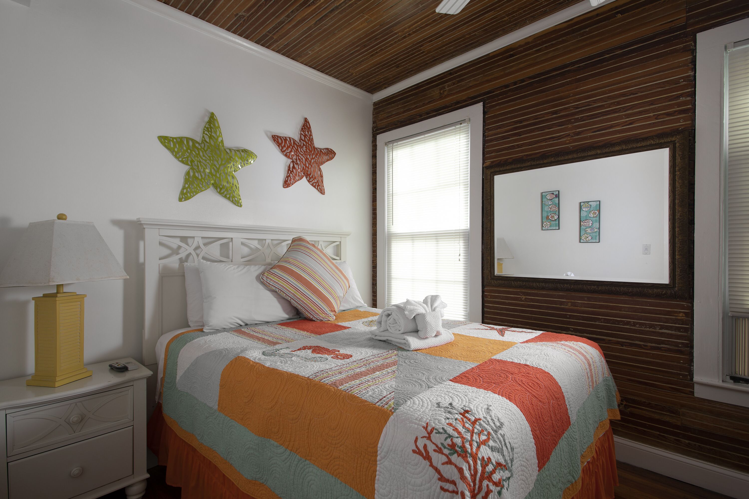 Une chambre à coucher avec un lit, une table de chevet, une lampe et des étoiles de mer décoratives accrochées au mur.