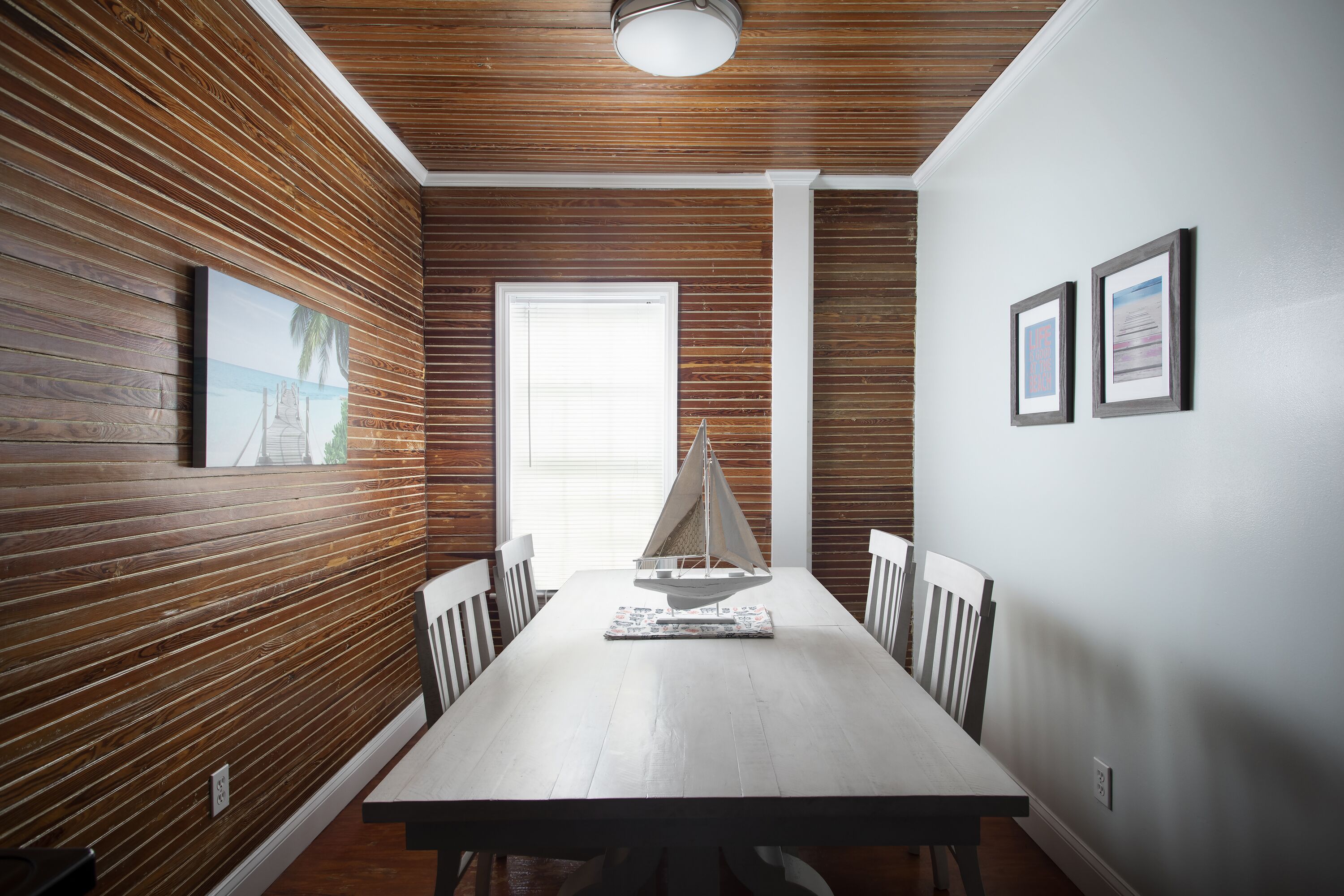 Un coin repas avec un mur lambrissé en bois, un plafond blanc et une maquette de voilier posée sur la table.