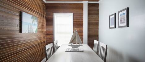 A dining area with a wooden paneled wall, a white ceiling, and a sailboat model on the table.