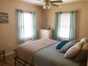 Une chambre à coucher avec un lit, une commode et deux fenêtres avec des rideaux.