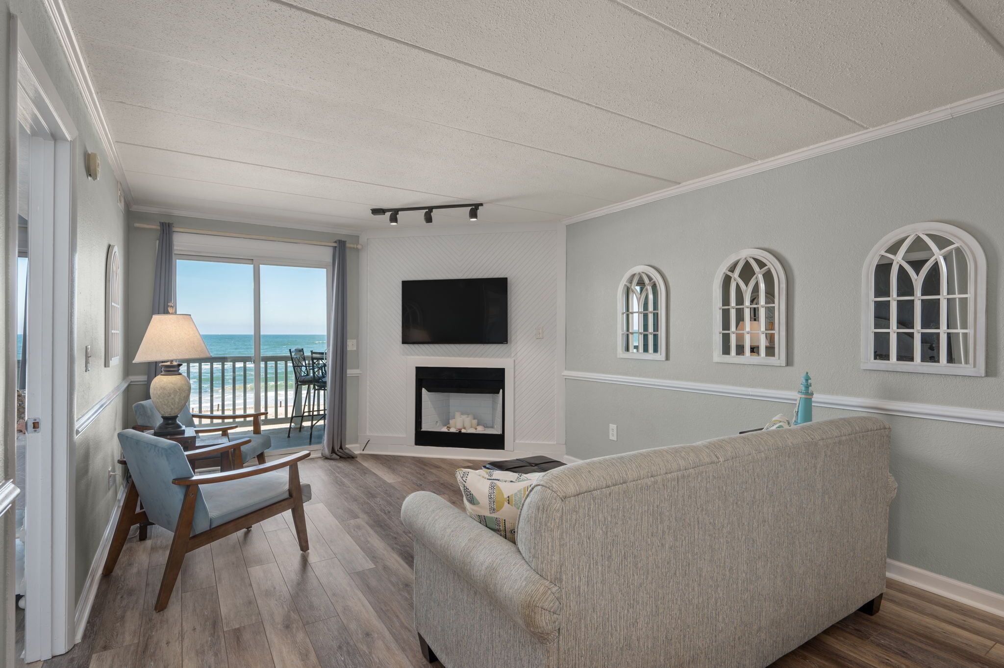 A living room with a fireplace, a sofa, a lamp, and a view of the ocean.