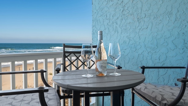 Une table avec une bouteille et deux verres, placée sur un balcon donnant sur la plage.