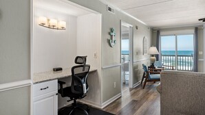 Une pièce comprenant un bureau, un fauteuil de bureau et offrant une vue sur l’océan grâce à de grandes fenêtres.