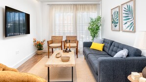 Ein modernes Wohnzimmer mit grauem Sofa, Holzstühlen, einem Couchtisch und einem an der Wand befestigten Flachbildfernseher.