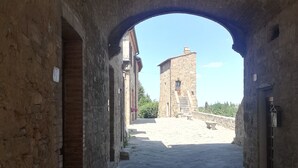 Ein gepflasterter Weg führt zu einem historischen Gebäude mit einem Turm, das von einem Bogenwerk eingefasst wird.