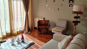 Ein Wohnzimmer mit Holzboden, einer Couch, einem Sessel, einem Tisch mit Dekoration, einer Wanduhr und einer Lampe.