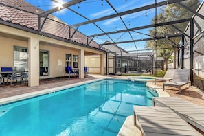 A swimming pool with lounge chairs, a covered patio, and a clear sky.