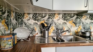 Une cuisine avec des armoires blanches, un évier en acier inoxydable et un pare-feu décoré de motifs de feuilles et de fleurs tropicales.
