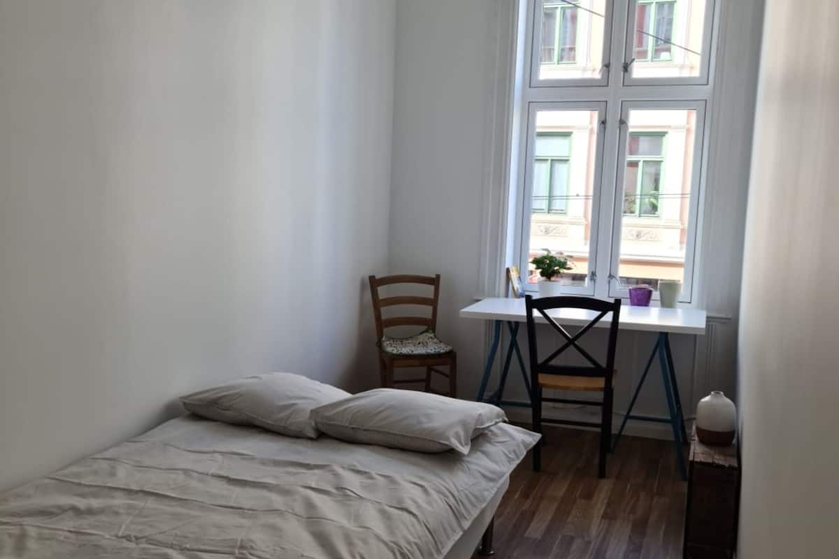 A small, clean room with a bed, a desk, and a window.