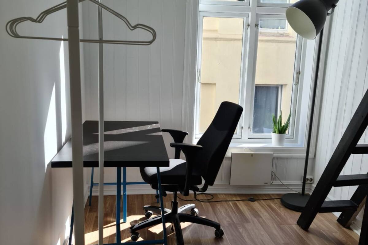 A room with a desk, office chair, and a hanging coat rack.