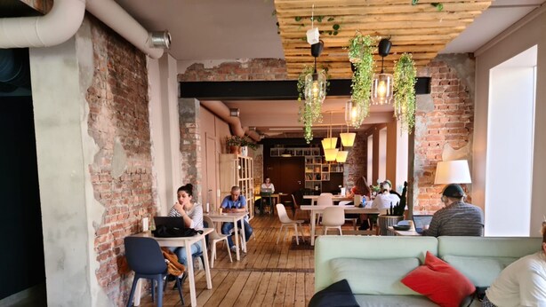 Un café chaleureux avec des murs en briques apparentes, des planchers en bois et des plantes suspendues.