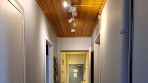 Un couloir étroit, doté d’un plancher en bois et de murs blancs, qui mène à une porte au fond.
