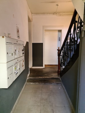 A narrow hallway with a staircase on the right, a row of utility cabinets on the left, and a door at the end.