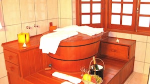 Une baignoire en bois, une serviette blanche, une bougie et un panier de fruits avec une bouteille de champagne.