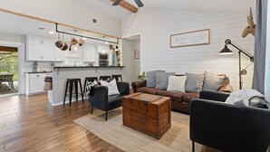 A spacious living area with a sofa, coffee table, and a kitchen in the background. - Farmhouse: Sleeps 6 | Soaking Tub | Fire Pit | Wimberley TX (Wimberley)