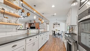 A modern kitchen with white cabinetry, a wooden countertop, and stainless steel appliances. - Farmhouse: Sleeps 6 | Soaking Tub | Fire Pit | Wimberley TX (Wimberley)