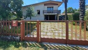 A two-story house with a balcony, surrounded by a metal fence and palm trees.