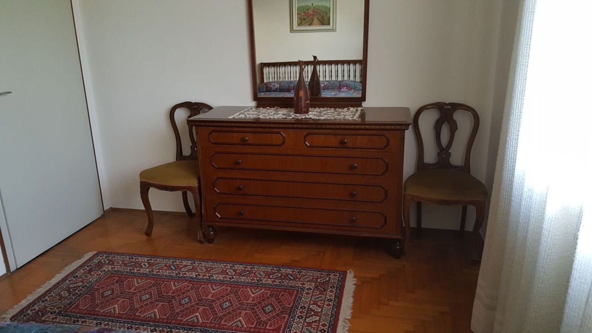 Una habitación con un aparador de madera, dos sillas, un tapete estampado y un cuadro en la pared.