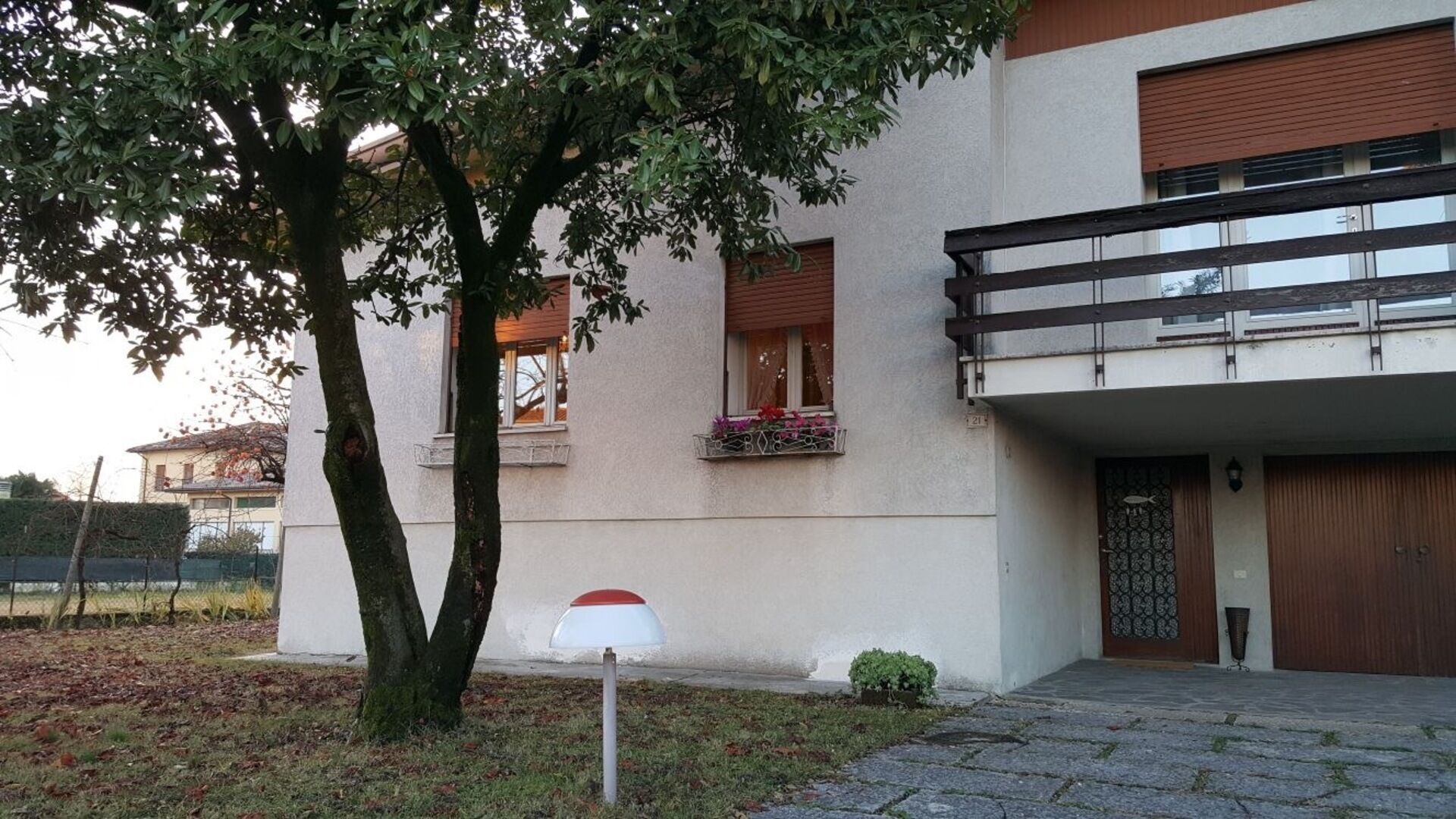 A modern building with a balcony, a mailbox, and a tree in front.