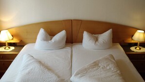 Un llit doble amb llençols blancs, dos almoines i dues làmpades de nit sobre taulells de fusta.