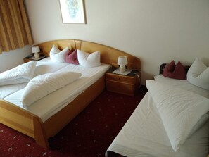 A double bed with white linens and multiple pillows, a wooden nightstand with a lamp, and a red carpeted floor. - Pension Weirather (Imst)