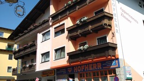 Un edifici d'alguns pisos amb balcons decorats amb flors, un rètol que diu "Hofherr Apartments Zimmer" i un rètol de "Pension".