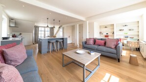 A modern living room with a grey sofa, wooden coffee table, and a kitchen area with a central island. - Dawson Place (London)