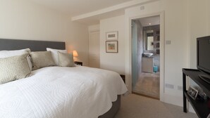 A hotel room with a large bed, a bedside table with a lamp, a TV, and a small cabinet. - Dawson Place (London)