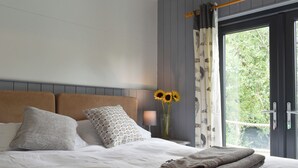 Un lit bien fait, avec des oreillers, un vase rempli de tournesols et une vue sur la verdure par la fenêtre.