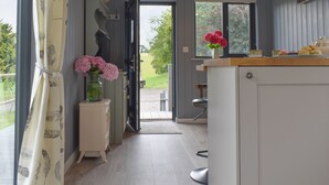 Une cuisine avec un comptoir en bois, un meuble blanc, un vase rempli de fleurs roses et une fenêtre donnant sur un paysage verdoyant.