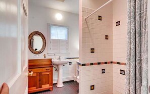 A bathroom with a wooden vanity, a pedestal sink, a mirror, and a shower area with tiled walls. - West Tisbury Inn (Vineyard Haven)