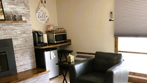 A living room with a fireplace, a coffee machine, a microwave, and a seating area with a sofa and a chair. - Cozy spacious king bed suite, In the heart of Historic Helena, Montana! (Helena)