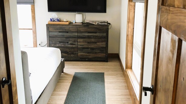 A bedroom with a bed, a dresser, a flat-screen TV mounted on the wall, and a wooden floor. - Cozy spacious king bed suite, In the heart of Historic Helena, Montana! (Helena)