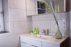 A bathroom with a white sink, a green glass bottle, and a vase with yellow flowers.