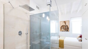 Une salle de bain moderne avec une douche à parois de verre, un lavabo blanc et un lit agrémenté d’une tête de lit décorative.