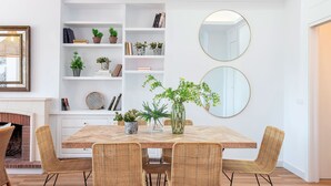 Uma sala de jantar com uma mesa de madeira, cadeiras de vime, uma estante branca e dois espelhos redondos na parede.
