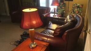 Ein Wohnzimmer mit einer Ledersofa, einem Holztisch, einer roten Stehlampe und einem kleinen Tisch mit einer Lampe.