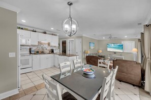 A modern kitchen with white cabinets, a dining table with chairs, a brown sofa, and a television mounted on the wall. - Nicely updated 2Bed 2Bath with Great Ocean Views  (Myrtle Beach)
