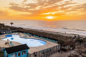 A beachside pool area with lounge chairs, a lifeguard tower, and a view of the ocean at sunset. - Nicely updated 2Bed 2Bath with Great Ocean Views  (Myrtle Beach)