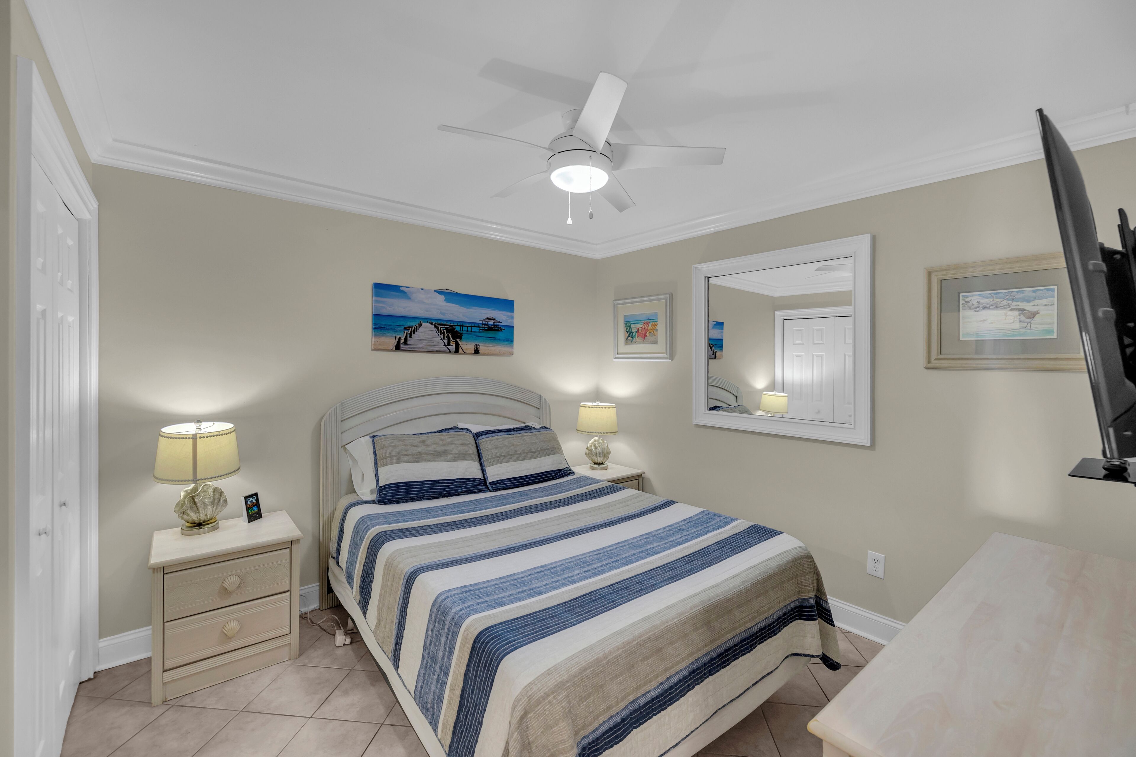A bedroom with a bed, nightstands, a ceiling fan, and wall art.