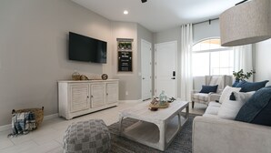 A modern living room with a flat-screen TV, a white sofa, a coffee table, and a white cabinet. - Luxury Heated Pool, Spa & Gym- 4BR Mesa Townhome (Mesa)