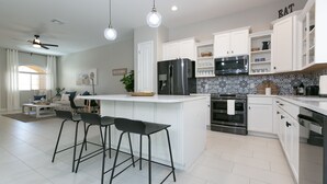 A modern kitchen with white cabinetry, a stainless steel refrigerator, a microwave, and a large island with bar stools. - Luxury Heated Pool, Spa & Gym- 4BR Mesa Townhome (Mesa)