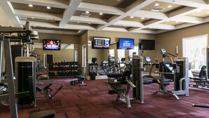 A gym with various exercise equipment, a television displaying a news program, and a digital screen with fitness information. - Luxury Heated Pool, Spa & Gym- 4BR Mesa Townhome (Mesa)