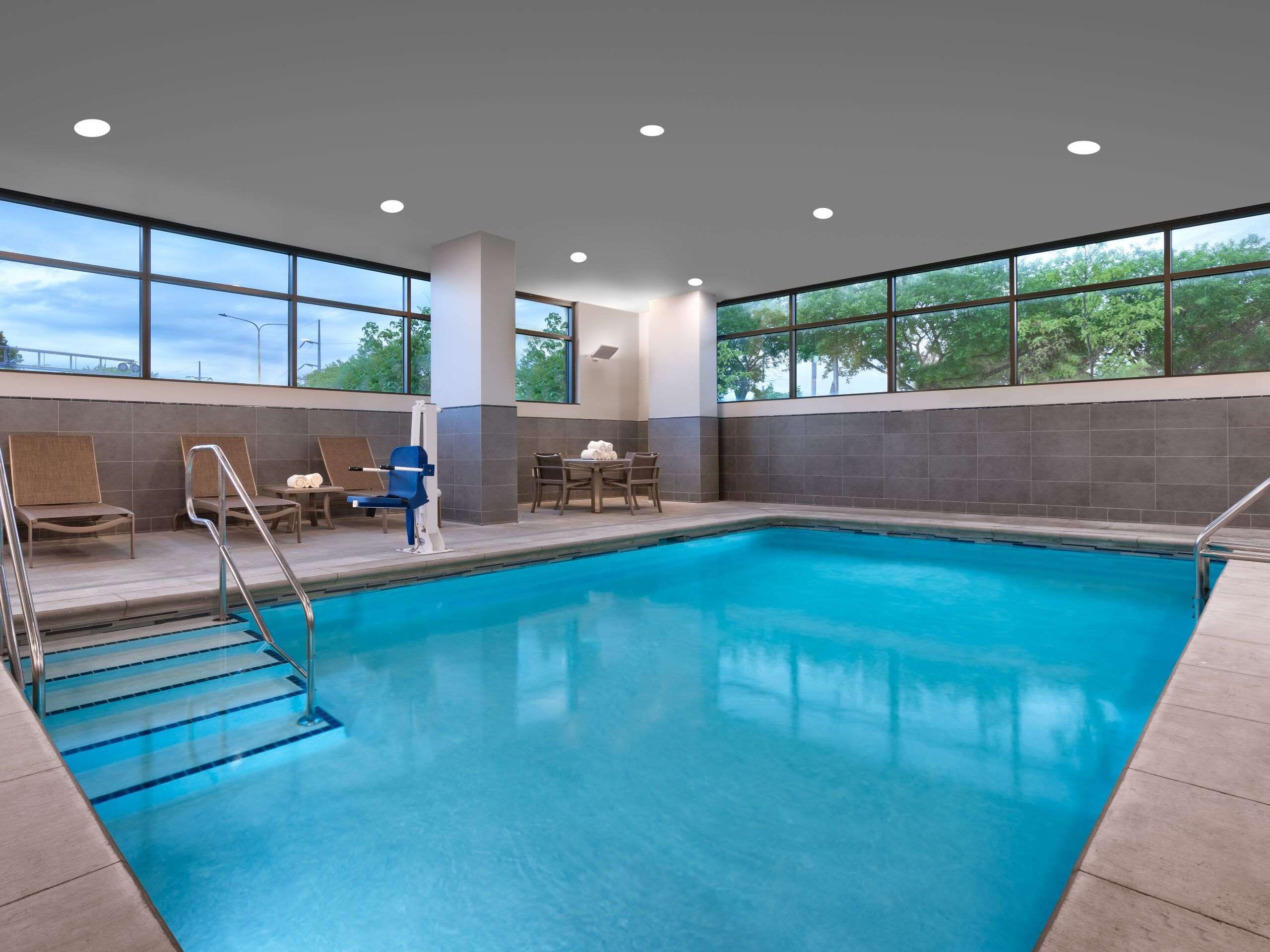 A swimming pool with steps leading into it, surrounded by lounge chairs and a table with towels.