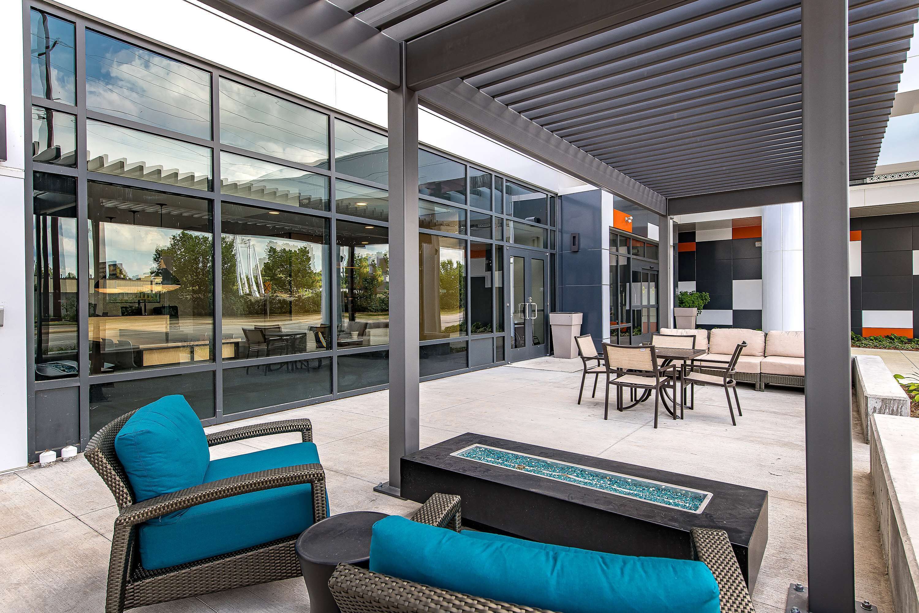 Een modern terras buiten met rieten meubilair, een glazen uitbouw en uitzicht op het omliggende landschap.